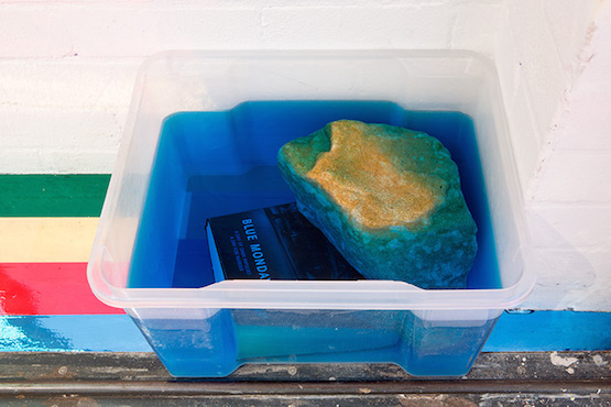 Jim Lambie, Blue Monday, 2015. Water, vodka, food dye, book, stone, plastic box. 26 × 45 × 36cm. Image