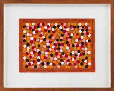 A framed painting on paper features pink, black, and white dots on brown paper.