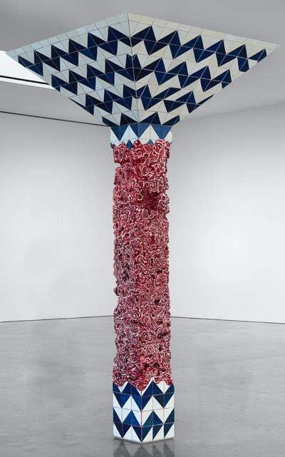 A blue and white-tiled pillar in the middle of a gallery space, with meat marbling texture painted on in the centre of it, an artwork by artist Adriana Varejão