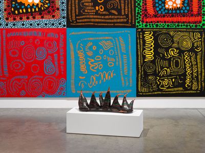 A large abstract painting by Yayoi Kusama is foregrounded by a sculpture made up of a row of spikes. The works are showing in a gallery space.