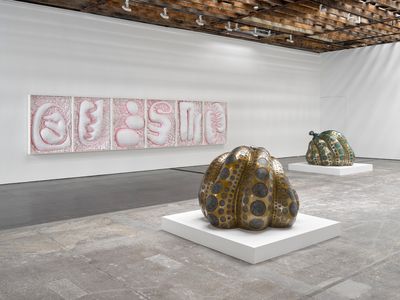Two pumpkin-shaped sculptures in the gallery space are gold and black, and foreground a pink and white abstract painting running along one of the far walls to the left of the gallery space.