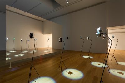 Simon Starling, Project for a Masquerade (Hiroshima), (2010–11). In collaboration with Yasuo Miichi, Osaka 16 mm film transferred to digital (25 minutes, 45 seconds), 8 wooden masks and bowler hat, metal stands, suspended screen/mirror, HD projector, media player, and speakers. Dimensions variable.