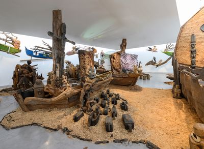 Kidlat Tahimik, Ang Ma-bagyong Sabungan ng 2 Bathala ng Hangin, A Stormy Clash Between 2 Goddesses of the Winds (WW III – the Protracted Kultur War) (2019). Wooden carved icons, ritual objects, interwoven C-print photographs, projected images, audio, mosaic, rattanbasket figurines, back-strap bamboo loom, wrought-iron launch-pads, fibreglass, root sculptures, rotten fishing boats, sawdust, bamboo fences and runo-reed fauna. Dimensions variable. Exhibition view: Leaving the Echo Chamber, Sharjah Biennial 14 (7 March–10 June 2019). Commissioned by Sharjah Art Foundation. Courtesy the artist. Photo: Sharjah Art Foundation