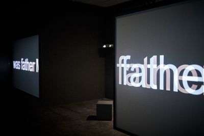 Dual screen installation in dark space reading 'Father' in blurred letters