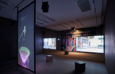 Three video screen installation in dark room in front of painted mural
