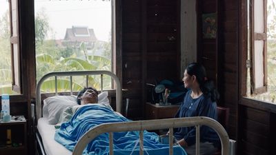 Film still woman sits at bedside of man in wooden cabin