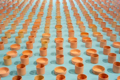 A series of light brown vessels of varying heights are placed on a light-blue surface as part of an installation by Cooking Sections.