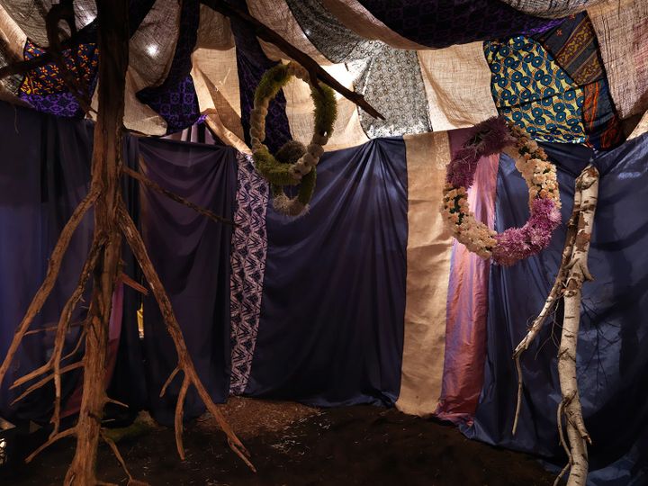 A tent-like structure photographed from inside, showing two flower wreaths hanging from the ceiling and two class=
