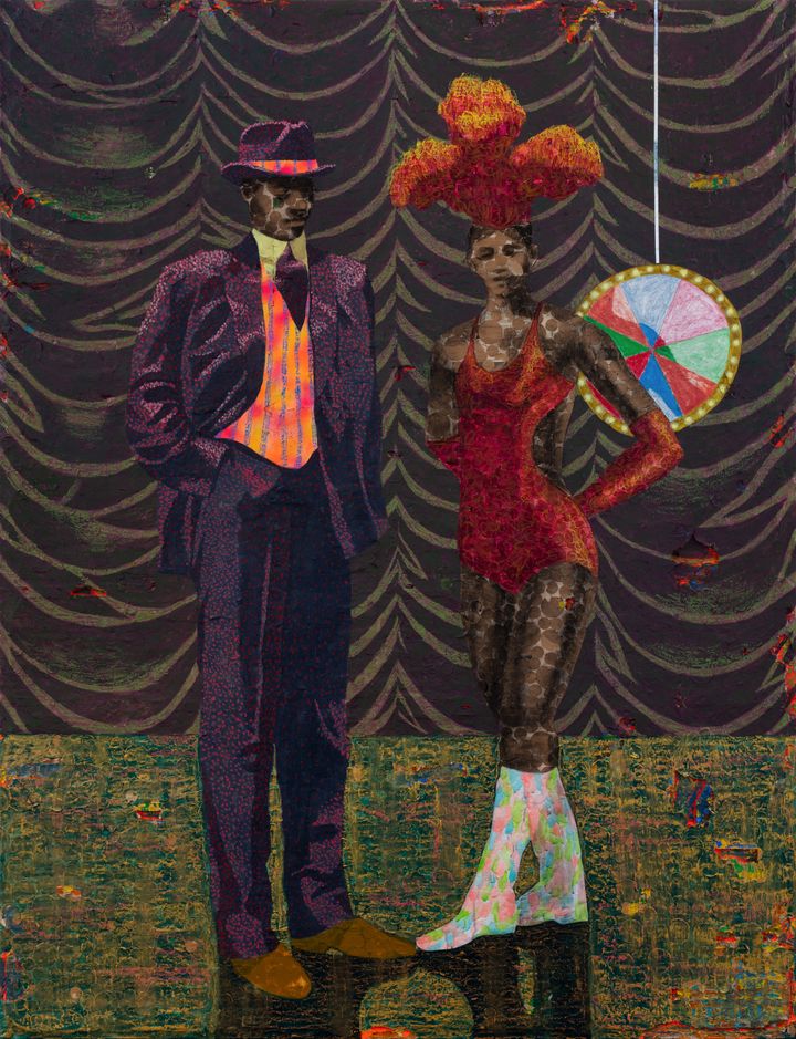 A man and woman stand on a stage. The man is in a purple suit and bowler hat, while the woman is in an orange bodice with feathers on her class=