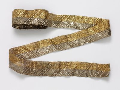 A pattern, silver gilded ribbon belonging to the Victoria & Albert Collection is photographed against a grey background.