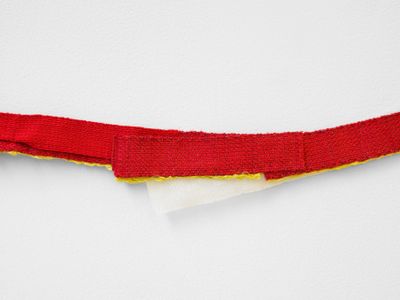 A close-up shot of a textile work by Hana Miletić features a strip of red textile hanging against a white wall.