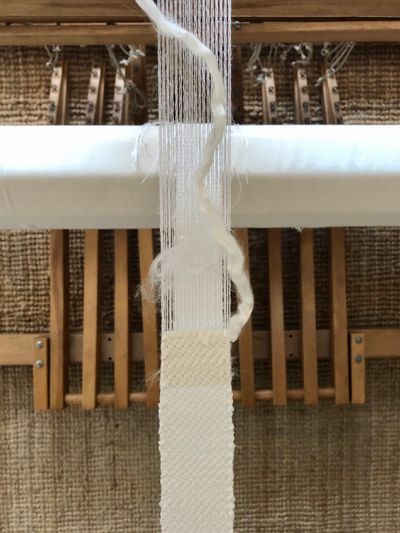 A close-up photograph of thread being woven on the loom.