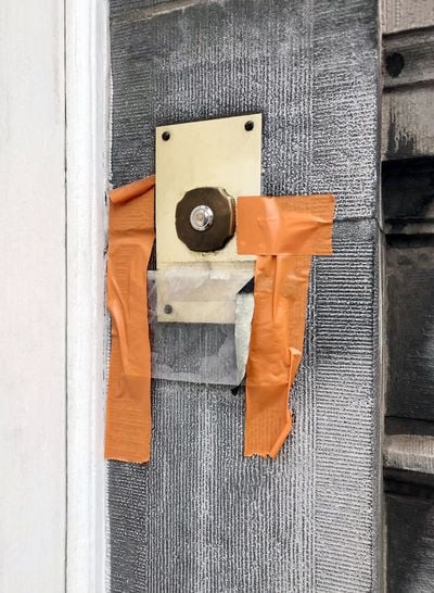 Orange tape surrounds a doorbell. The image inspired the creation of Hana Miletić's orange, fragmentary textile work.