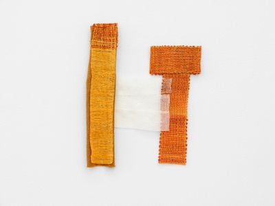 A fragmentary orange textile piece by Hana Miletić is photographed hanging on the wall.