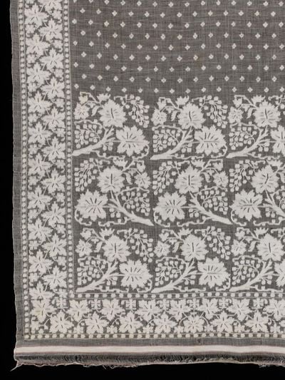 A segment of fine muslin cloth with repeated floral patterns on it in white is photographed up close.
