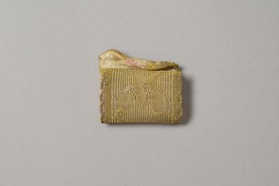 A gold silk folding needle case from the Victoria & Albert collection is photographed against a grey background.