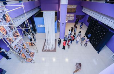 An aerial shot of textile works showing at the Dhaka Art Summit of 2018, in a gallery space with purple walls.