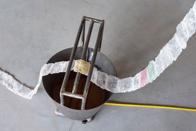 Installation showing a line of multicolour fabric hanging across a metal bucket.