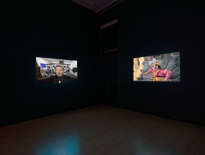 Two screens in a darkened gallery space show the artist Lu Yang to the left, while the right-hand screen shows a Balinese traditional dancer.