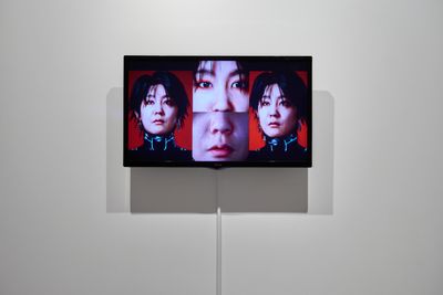A screen in the gallery space is split in four, showing different angles of the artist Lu Yang's face.