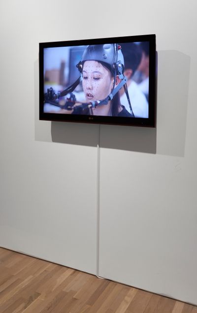 A screen in the gallery space shows the artist Lu Yang with motion capture technology registering her facial movements.
