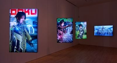 A series of four screens in the gallery space show a figure in each in a futuristic landscape.