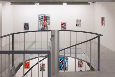 A photograph of a white gallery space captures a stairwell in the foreground, behind which the upper and lower floors are visible, and in them, a series of closely cropped photographs of brightly coloured kimonos that hang along the walls.