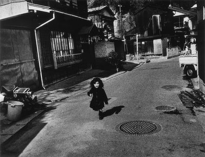 A black and white photograph by Miyako Ishiuchi captures a small child running through the street in Yokosuka, Kanagawa.