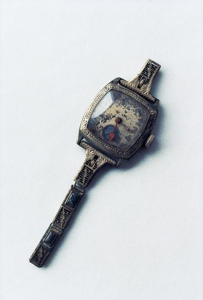 A damaged watch photographed by Miyako Ishiuchi up close against a white background.
