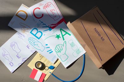 The contents of 'Home-Kit' an educational initiative organised by de Appel in Amsterdam, are spilled out. Pages featuring hands outlining the sign language alphabet are strewn around a cardboard box.