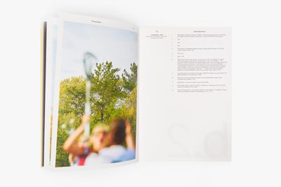 An exhibition publication produced by de Appel is photographed with the pages open. A page of text is visible to the right, while the left features a blurred image of children playing with a large bubble maker.