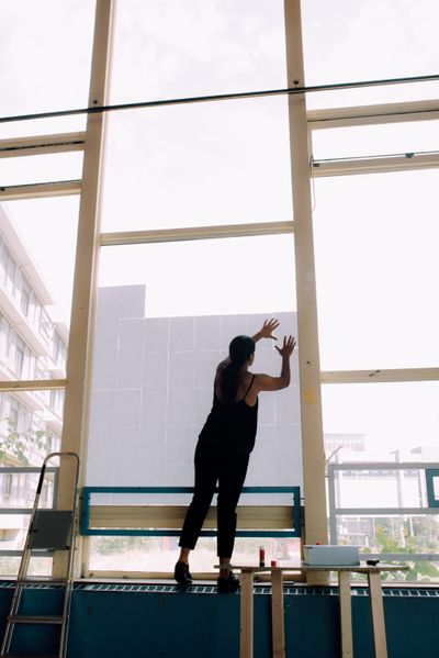Farah Fayyad performs a spatial intervention at de Appel. She is pictured placing sheets of paper on a window.