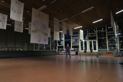 In a dim exhibition hall, the artist Georgia Sagri dances below a series of white flags hanging from the ceiling, each of which has an abstract human figure drawn on its surface.