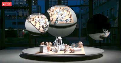 A series of sculptures on a circular platform are flanked by two circular mirrors that reflect the artworks. The image is a screen capture of a live stream by de Appel.