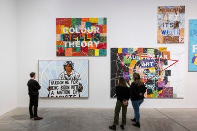 A group of four abstract paintings by Richard Bell in the gallery space with text in capital letters written across each of their surfaces, such as, 'Pardon me for being born into a nation of racists' and  'Bell's colour theory'