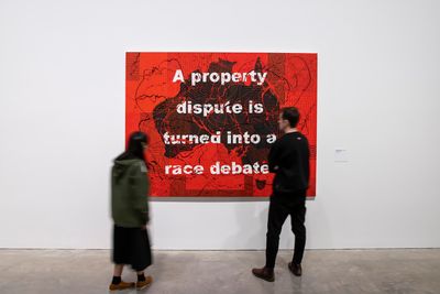 A painting of Australia by Richard Bell painted black against a red background, with the words 'A property dispute is turned into a race debate' written in capitals across the surface