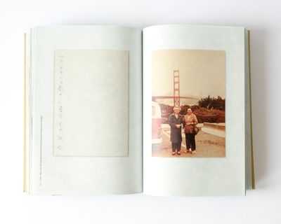 Open book showing a postcard with a line of text besides an image of couple standing in front of a bridge.
