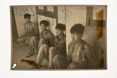 Sepia print showing four young men sitting on the ground. 