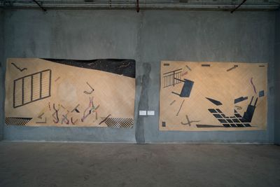 Two black and beige mats are shown on a grey concrete wall. In black, tables are featured, some of them fragmented so that the pieces are distributed across the picture planes. 