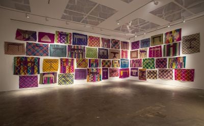 Colourful patterned mats are hung along two adjoining walls in a cluster at Silverlens' dimly lit gallery.