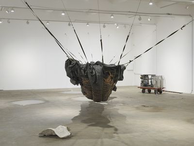 An installation in the gallery space by Yu Ji, featuring a black hammock-like structure made from tarpaulin and netting, hanging across the gallery space, as well a a machine made up of two milk canisters placed on a trolley.