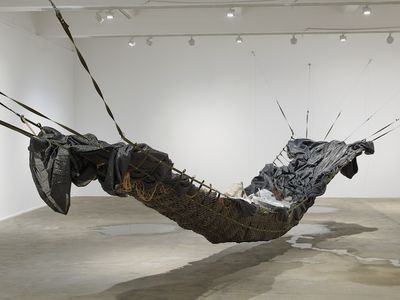 An installation by Yu Ji in the gallery space, featuring a large hammock made of netting and black tarpaulin in the gallery space, with a pool of water beneath it.