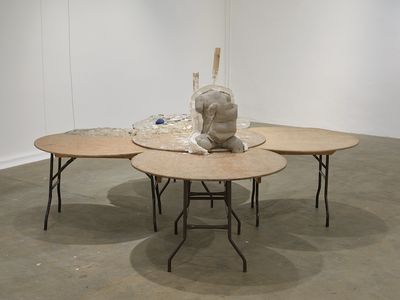 An installation in the gallery space by Yu Ji, featuring five overlapping round tables. In the centre, a cement torso sits upright.