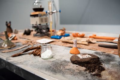 Candice Lin, La Charada China (Tobacco Version) (2019). Cement with casein paint, welded steel table frame, tobacco, ceramics, distillation system (distilling a tincture of tobacco, sugar, tea, and poppy), poppy pod putty, sugarcane, white sugar, cacao, sage, ackee, oak gall, Anadenanthera, dong quai, California clay, Dominican Republic clay, metal parts, bucket, pumps, tubing, dried indigo, glass slides, bottles, drawings, tile, rubber, wood. Exhibition view: The Agnotology of Tigers, LSUMOA, Louisiana (20 October 2021–20 March 2022).