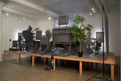 Stephanie Syjuco, Neutral Calibration Studies (Ornament + Crime) (2016). Wooden platform, neutral grey seamless backdrop paper, digital adhesive prints on lasercut wooden props, dye-sublimation digital prints on fabric, items purchased on eBay and craigslist, photographic prints, artificial plants, live plants, neutral calibrated gray paint. 25.4 x 50.8 x 20.32 cm.