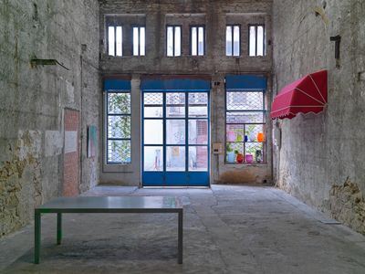 A sparse but well lit gallery space shows an exhibition of works by Christodoulos Panayiotou, including red awning attached to the wall to the right and a table in the foreground.