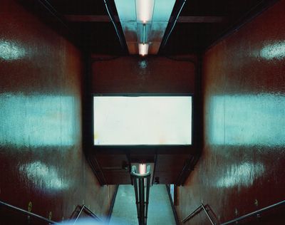 A photograph by Christopher Button features a clean, red stairwell of Central divided by a handrail, an over-exposed, white advertising screen bathing the scene in a cinematic, electric blue.