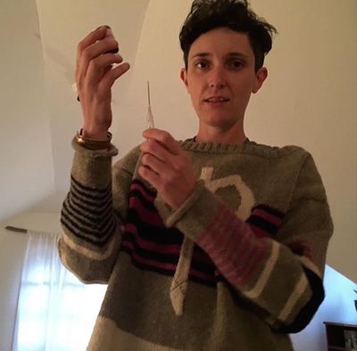 A participant in Ellen Lesperance's Congratulations and Celebrations project is pictured about to take hormone medicine, wearing a sweater that features a labrys battle axe. 