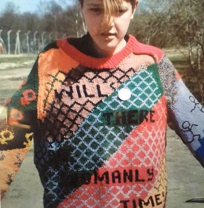 An archival colour photograph of a Greenham Common protester in a sweater that reads 'Will There Be Womanly Times?'
