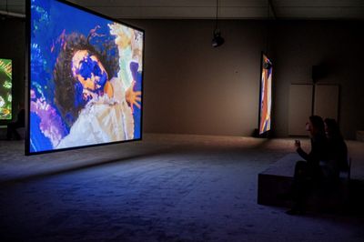 Video installation screen showing dancing woman with purple paint on her face.